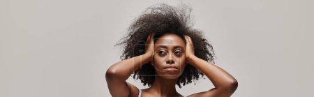 Foto de Una mujer afroamericana con el pelo rizado lo sostiene delante de su cara, creando un efecto velo. - Imagen libre de derechos
