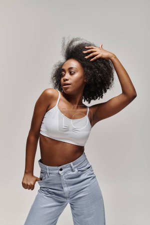 Téléchargez les photos : Une femme afro-américaine élégante aux cheveux bouclés pose en toute confiance dans un haut blanc et un jean. - en image libre de droit