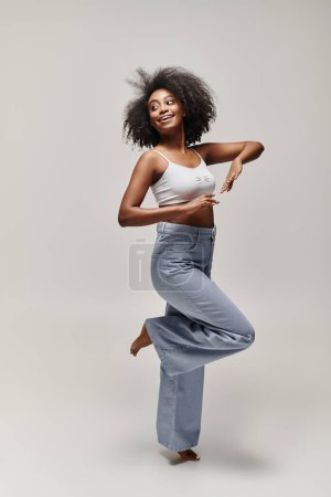 Young African American woman with curly hair performing a pose in a white tank top.