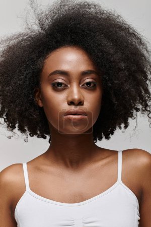 Eine stylische Afroamerikanerin mit voluminösem Afro posiert selbstbewusst für ein Porträt in einem Studio-Setting.