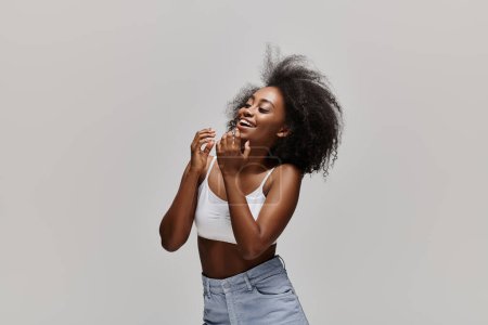 A stunning African American woman with curly hair poses elegantly in a white top and denim skirt, exuding grace and style.