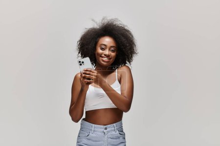 Eine junge Afroamerikanerin mit lockigem Haar hält ein Handy in den Händen, das in seinen Bildschirm vertieft ist.