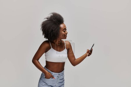 Belle femme afro-américaine aux cheveux bouclés profondément absorbée par l'utilisation d'un téléphone portable.