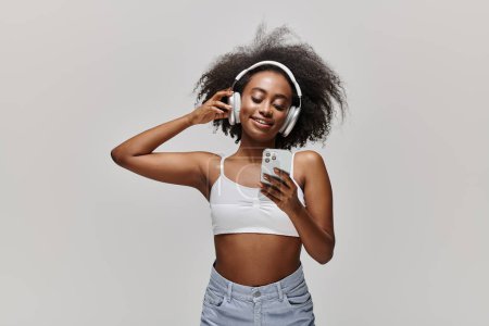 Photo for Young African American woman with curly hair, wearing headphones, immersed in the tunes shes listening to. - Royalty Free Image
