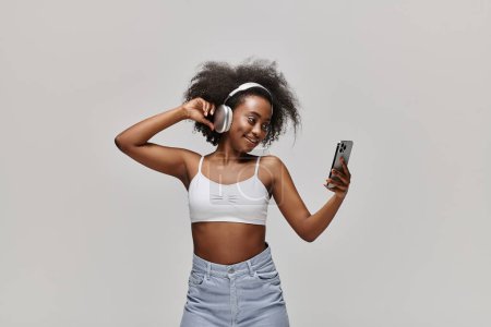 Une femme afro-américaine magnifique dans un haut blanc tient élégamment un téléphone portable.