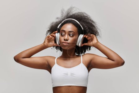 Foto de Una joven afroamericana con el pelo rizado escucha música a través de auriculares. - Imagen libre de derechos