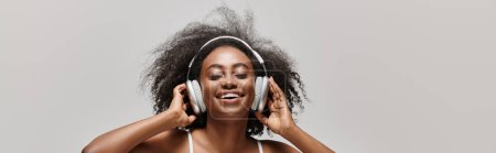 Una joven afroamericana con el pelo rizado usando auriculares, perdida en la música.