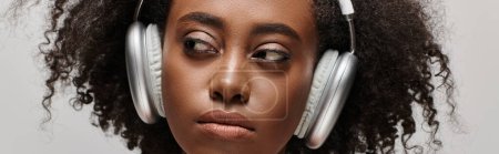 Photo for A beautiful young African American woman with curly hair wearing headphones over her face, immersed in music. - Royalty Free Image