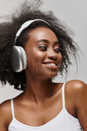 A young African American woman with curly hair smiles while wearing headphones.