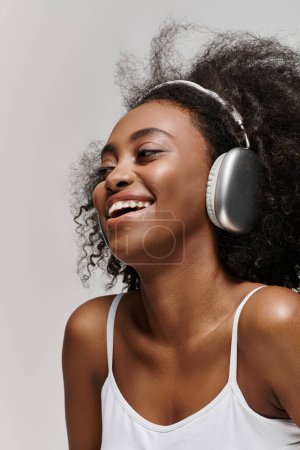 A radiant African American woman with curly hair, smiling as she listens to music through headphones.