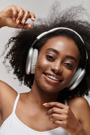 Foto de Joven mujer afroamericana con el pelo rizado escuchando música a través de auriculares, sintiendo el ritmo. - Imagen libre de derechos