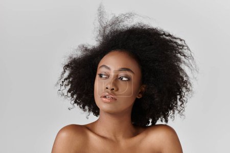 A beautiful young African American woman with curly hair poses confidently for a portrait in a studio setting.