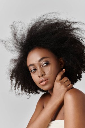 Eine schöne junge Afroamerikanerin mit lockigem Haar posiert selbstbewusst für einen Fotografen in einem Studio.