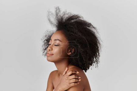 Una hermosa joven afroamericana con el pelo rizado está desnuda mientras su cabello cae en cascada en el viento, exudando gracia y belleza.