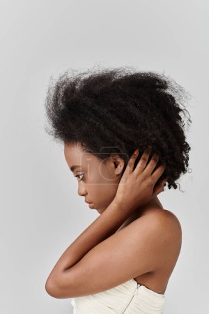 A beautiful young African American woman in a white dress delicately holds and caresses her curly hair.