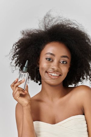 Eine atemberaubende junge Afroamerikanerin mit lockigem Haar präsentiert eine Flasche Haarprodukt in einem lebendigen Studio-Setting.