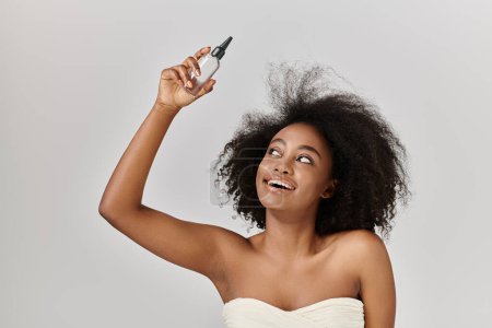 A beautiful African American woman with curly hair holds a bottle of hair product