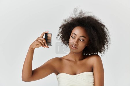 A stunning African American woman with curly hair, wearing a white dress, holding a compact in a skin care concept.