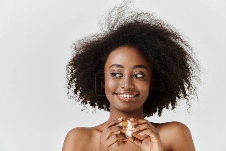 Foto de Una joven y hermosa mujer afroamericana con el pelo rizado sostiene un frasco de crema, encarnando el concepto de nutrición y autocuidado. - Imagen libre de derechos