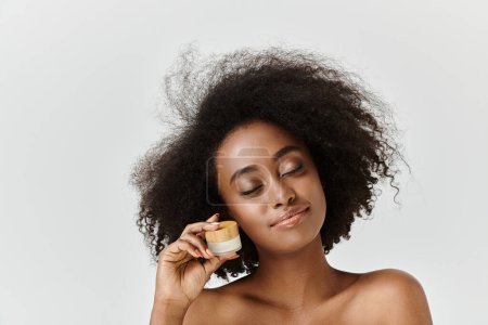 Una hermosa joven afroamericana con el pelo rizado sosteniendo un frasco de crema en su mano derecha.