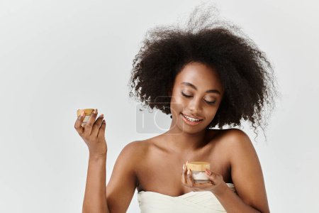 Photo for A stunning young African American woman, wrapped in a towel, holds a jar with cream - Royalty Free Image