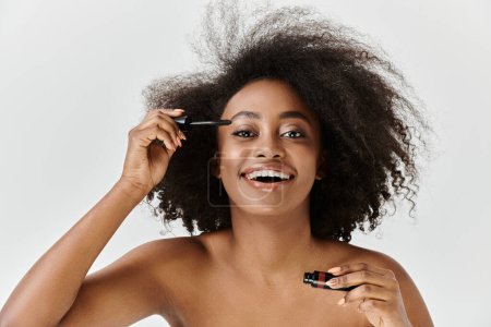 A beautiful young African American woman with her curly hair in a studio setting, applying mascara