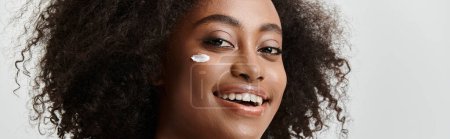 Eine schöne junge Afroamerikanerin mit lockigem Haar, die mit einem strahlenden Lächeln reines Glück vermittelt.