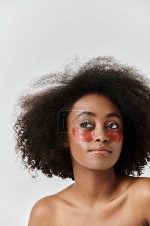 A striking African American woman with curly hair wearing a vibrant red eye patch, showcasing a unique and bold skin care concept.