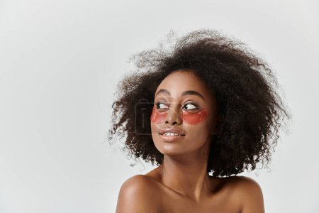 Photo for A beautiful young African American woman with curly hair, showcasing striking red eye patch in a studio setting. - Royalty Free Image