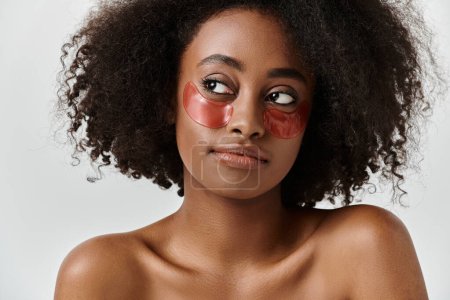 Téléchargez les photos : Une belle jeune afro-américaine aux cheveux bouclés portant un bandeau rouge frappant dans un décor de studio. - en image libre de droit