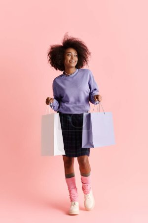 Eine junge Afroamerikanerin mit lockigem Haar lächelt, während sie im Studio Einkaufstüten in der Hand hält.