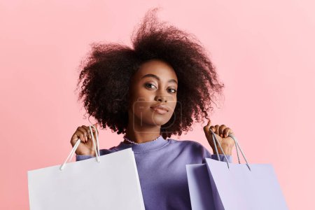A glamorous African American woman with curly hair holds multiple shopping bags in a studio setting.