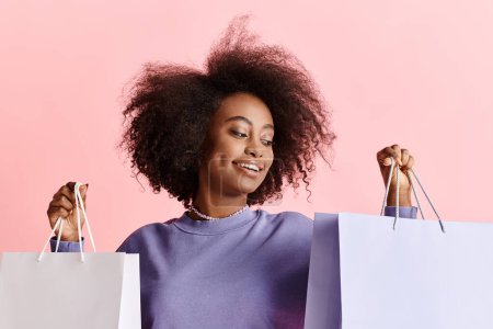 Photo for A beautiful young African American woman with curly hair stands smiling, holding shopping bags. - Royalty Free Image