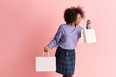 Stylish young African American woman with curly hair, wearing a purple shirt and plaid skirt, holding shopping bags.