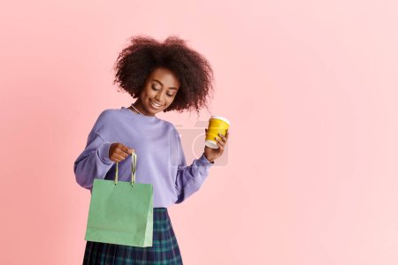 Photo for A beautiful African American woman with curly hair holding a cup and a paper bag. - Royalty Free Image