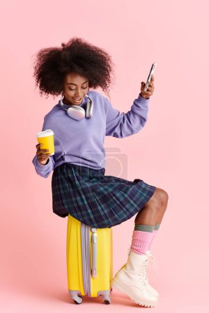 Eine schöne junge Afroamerikanerin mit lockigem Haar sitzt auf einem Koffer, eingetaucht in ihren Handybildschirm.