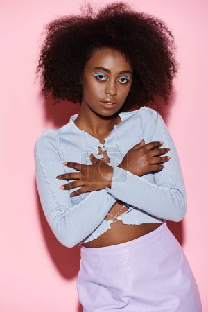 Una joven y elegante mujer afroamericana con un afro de pie con confianza frente a un vibrante fondo rosa.