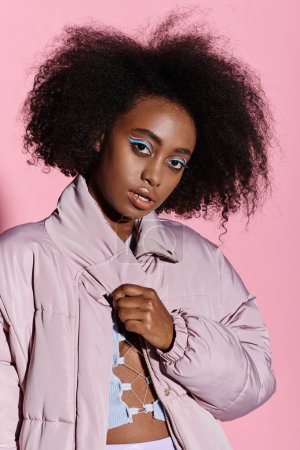 Stylish African American woman with curly afro hair posing in front of a vibrant pink background.
