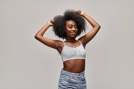 Eine stylische junge Afroamerikanerin mit lockigem Afro-Haar posiert selbstbewusst vor der Kamera in einem Studio-Setting.