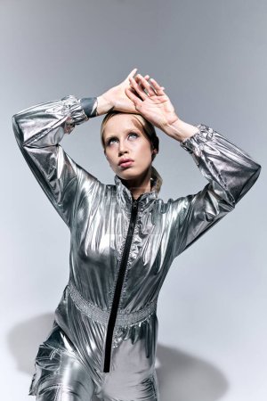 Téléchargez les photos : Modèle féminin fantaisie en argent tenue inhabituelle posant en mouvement sur fond gris et détournant les yeux - en image libre de droit