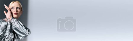Téléchargez les photos : Femme chic en argent tenue inhabituelle posant en mouvement sur fond gris et détournant les yeux, bannière - en image libre de droit