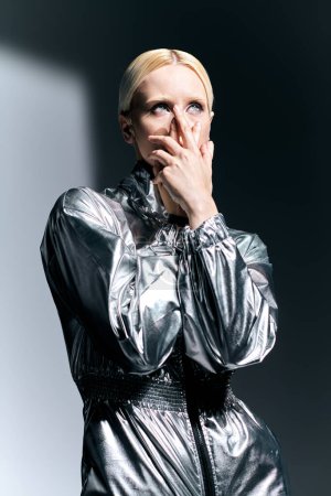 Téléchargez les photos : Femme blonde extraordinaire en costume robotique argenté posant en mouvement et détournant les yeux, fond gris - en image libre de droit