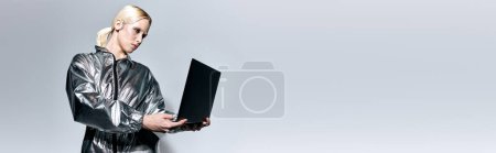 Téléchargez les photos : Femme extraordinaire avec maquillage en vêtements futuristes en regardant son ordinateur portable sur fond gris, bannière - en image libre de droit