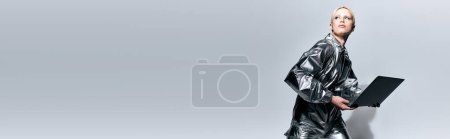 Photo for Attractive peculiar woman in robotic clothing posing in motion with laptop and looking away, banner - Royalty Free Image