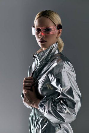 appealing blonde woman with futuristic glasses in silver outfit looking at camera on gray background