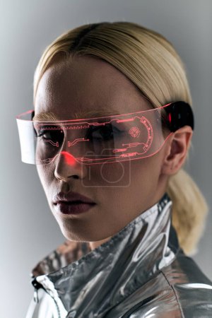 Téléchargez les photos : Séduisante femme blonde avec des lunettes futuristes en tenue argentée regardant la caméra sur fond gris - en image libre de droit