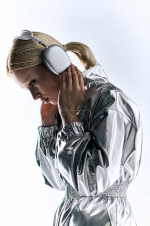 Téléchargez les photos : Modèle féminin particulier attrayant avec écouteurs portant une tenue robotique argentée et appréciant la musique - en image libre de droit