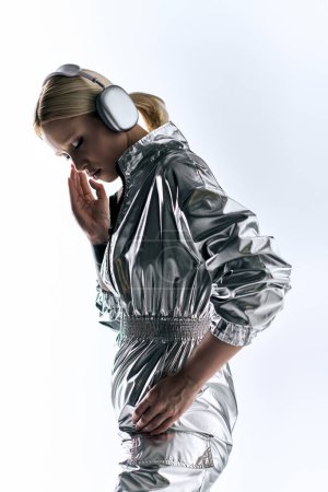 Téléchargez les photos : Attrayant modèle féminin bizarre avec écouteurs portant des vêtements robotiques en argent et appréciant la musique - en image libre de droit