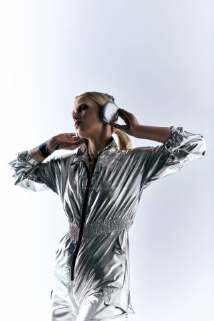 Téléchargez les photos : Femme belle extravagante avec écouteurs modernes en tenue futuriste argentée appréciant la musique - en image libre de droit