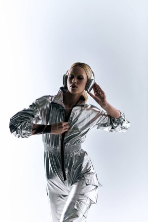Téléchargez les photos : Femme belle extravagante avec écouteurs modernes en tenue futuriste argentée appréciant la musique - en image libre de droit